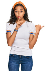 Young african american girl wearing casual clothes asking to be quiet with finger on lips pointing with hand to the side. silence and secret concept.