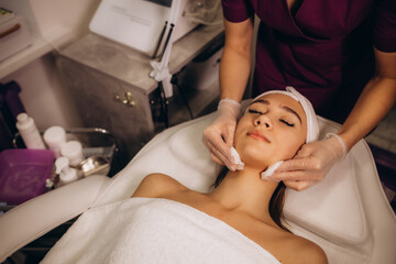 people, beauty, spa, cosmetology and relaxation concept - close up of beautiful young woman lying with closed eyes having face cleaning by sponge in spa