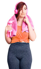 Young beautiful woman wearing sportswear and headphones holding bottle of water serious face thinking about question with hand on chin, thoughtful about confusing idea
