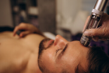 Professional beautician performing face needle-free mesotherapy for male patient at cosmetology