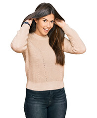 Young brunette woman wearing casual winter sweater smiling pulling ears with fingers, funny...