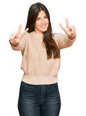 Young brunette woman wearing casual winter sweater smiling with tongue out showing fingers of both hands doing victory sign. number two.