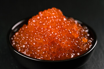 Red Caviar in a black bowl over black background.