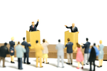 Miniature tiny people toy figure photography. Two men candidate public debate at tribune podium stage with a crowd of spectators. Isolated on white background