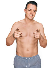 Fototapeta premium Handsome young man wearing swimwear shirtless pointing fingers to camera with happy and funny face. good energy and vibes.
