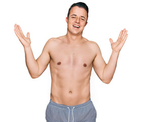 Fototapeta premium Handsome young man wearing swimwear shirtless celebrating crazy and amazed for success with arms raised and open eyes screaming excited. winner concept