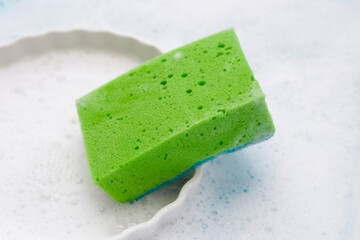 Plate with cleaning sponge in foam of dishwashing liquid. Washing dishes concept