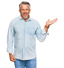 Middle age grey-haired man wearing casual clothes smiling cheerful presenting and pointing with palm of hand looking at the camera.