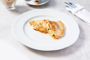 Pancakes with banana on a white plate in a cafe, restaurant.