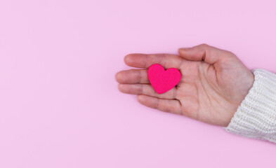 Fototapeta premium Woman's hands hold a pink heart on a pink background. Banner. Copy space. Top view. Selective focus.