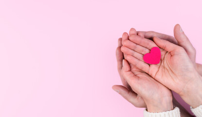 Woman's and man's hands hold a pink heart on a pink background. The concept of love, family and...