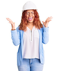 Young latin woman wearing architect hardhat celebrating mad and crazy for success with arms raised and closed eyes screaming excited. winner concept