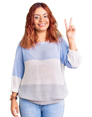 Young latin woman wearing casual clothes smiling looking to the camera showing fingers doing victory sign. number two.