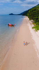 Fototapeta premium A beautiful view of a calm beach with crystal clear water on the blue sky at Koh Libong, Trang province, Thailand, Andaman Sea. A couple of men and woman walking on the beach