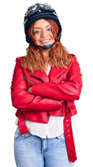 Young latin woman wearing leather jacket holding motorcycle helmet happy face smiling with crossed arms looking at the camera. positive person.