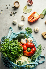 Various healthy organic vegetables in blue mesh grocery bag on kitchen table , top view. Healthy food cooking ingredients