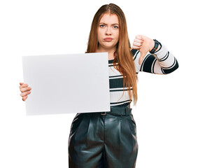 Young beautiful redhead woman holding blank empty banner with angry face, negative sign showing...