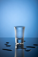 Colorless freezing cold alcohol drink in a frosty shot glass on a dark reflective tabletop with...