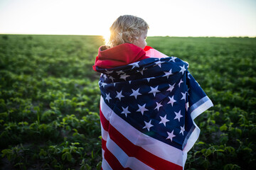 girl with an American flag in the background of sunset. Rays of the sun on green field of soybeans. Patriotic Holiday.