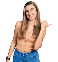 Hispanic young woman wearing casual summer shirt smiling with happy face looking and pointing to the side with thumb up.