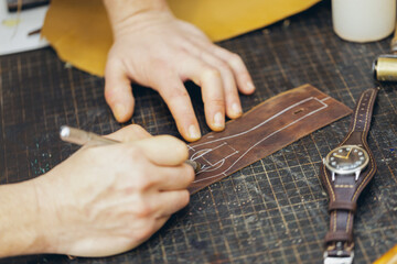 Close up of a shoemaker or artisan worker hands. Leather craft tools on old wood table.