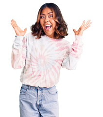 Young beautiful mixed race woman wearing casual tie dye sweatshirt celebrating crazy and amazed for success with arms raised and open eyes screaming excited. winner concept