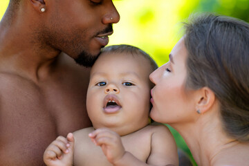 Mixed race family outdoor portrait. Mixed race parents with baby child on nature. Mixed race Portrait of happy african american or hispanic father and caucasian mother with mixed race baby.