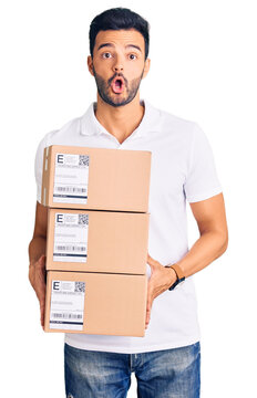 Young handsome hispanic man holding delivery package scared and amazed with open mouth for surprise, disbelief face