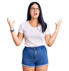 Obraz na płótnie Canvas Young beautiful asian girl wearing casual clothes and glasses crazy and mad shouting and yelling with aggressive expression and arms raised. frustration concept.
