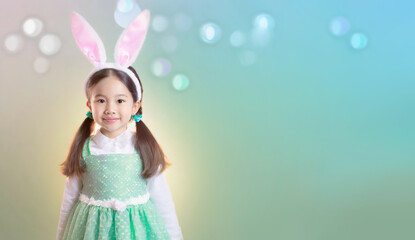 Obraz na płótnie Canvas Asian little girl wearing bunny ears on colorful background with bokeh, blank space for text