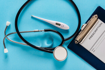 Clipboard with blank receipt form, stethoscope and thermometer on blue background