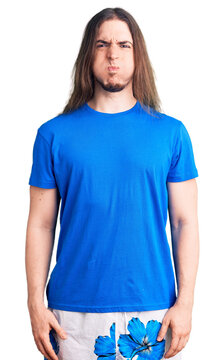 Young adult man with long hair wearing swimwear puffing cheeks with funny face. mouth inflated with air, crazy expression.