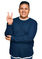 Fototapeta premium Young latin man wearing casual clothes smiling with happy face winking at the camera doing victory sign. number two.