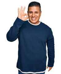 Young latin man wearing casual clothes smiling positive doing ok sign with hand and fingers. successful expression.