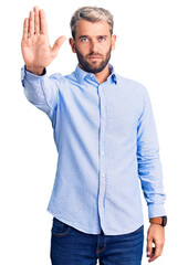Naklejka premium Young handsome blond man wearing elegant shirt doing stop sing with palm of the hand. warning expression with negative and serious gesture on the face.