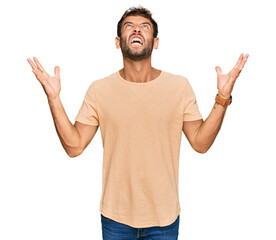 Handsome young man with beard wearing casual tshirt crazy and mad shouting and yelling with aggressive expression and arms raised. frustration concept.