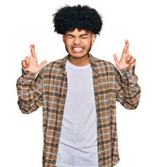 Young african american man with afro hair wearing casual clothes gesturing finger crossed smiling with hope and eyes closed. luck and superstitious concept.