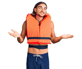 Young handsome man wearing nautical lifejacket clueless and confused expression with arms and hands...