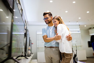 Young couple in consumer electronics store looking at latest digital devices, television.