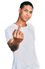Young hispanic man wearing casual white t shirt showing middle finger, impolite and rude fuck off...