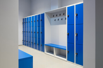 A row of blue lockers on a wall with key in a lock and a bench