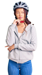 Young beautiful chinese girl wearing bike helmet serious face thinking about question with hand on chin, thoughtful about confusing idea