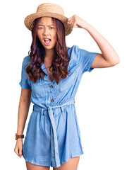 Young beautiful chinese girl wearing summer hat angry and mad raising fist frustrated and furious while shouting with anger. rage and aggressive concept.