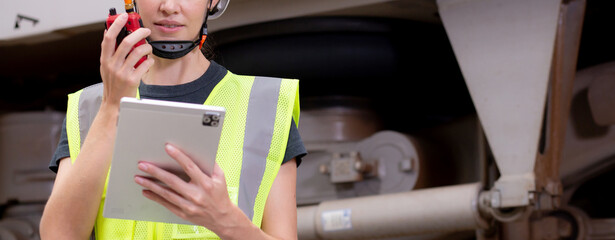 Young caucasian engineer woman using radio for command with worker checking electric train for planning maintenance and looking digital tablet in station, inspector check transport and infrastructure.