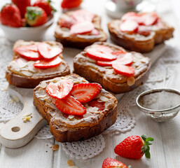 Bostocks a French pastry made of sliced brioche with frangipane cream, strawberries and almond flakes, sprinkled with powdered sugar on a white wooden table, close up view