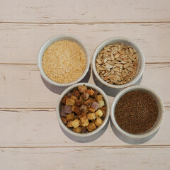 Grain seeds (white sesame, sunflower seed, chia seed and whole wheat dried bread) in four small white cups.