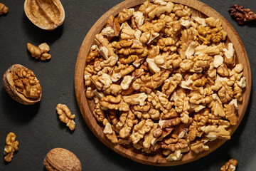 Wooden plate of walnut kernels on a black background, top view. Flat lay.