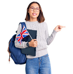 Young beautiful chinese girl wearing student backpack holding binder and uk flag smiling happy pointing with hand and finger to the side