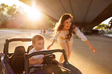 Mother having fun assisting son driving battery powered toy car