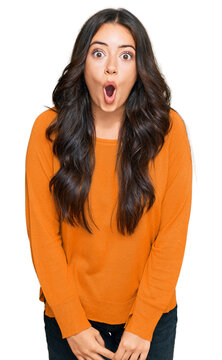 Beautiful brunette young woman wearing casual orange sweater scared and amazed with open mouth for surprise, disbelief face